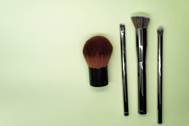 Cepillos de maquillaje profesionales con mango plateado sobre fondo verde con espacio para copiar. Concepto de belleza y cosmética facial
 - Foto, imagen