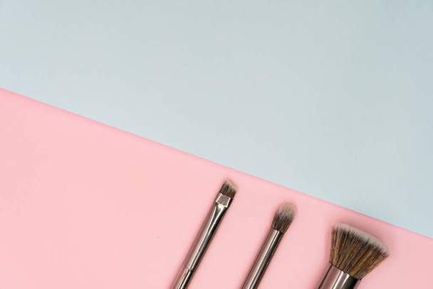 Cepillos de maquillaje profesionales con mango plateado sobre fondo rosa y azul con espacio para copiar. Concepto de belleza y cosmética facial
 - Foto, Imagen
