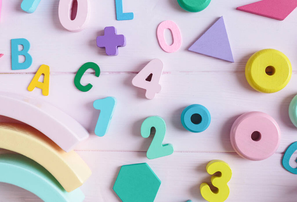 木製のおもちゃの虹、数字、ブロック、ピンクの背景にパステルカラーの弧。創造性の開発のための自然なプラスチック製のおもちゃ。フラットレイアウト、トップビュー。幼稚園、就学前の子供のための教育ゲーム - 写真・画像