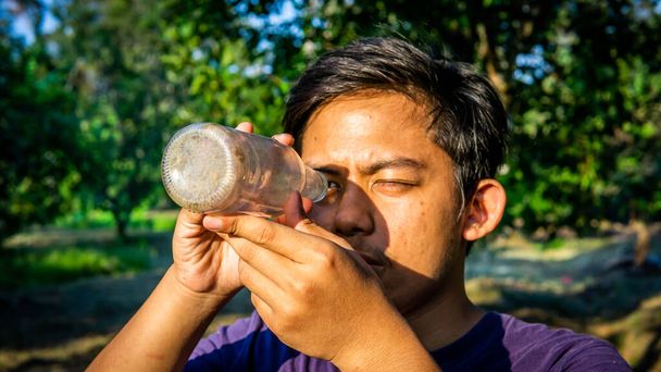 Muotokuva nuoresta malaijilaisesta, joka näkee lasipullon sisällä kiikarin, joka katselee aamun auringonnousua. Luonnon vihreä maisema tausta
. - Valokuva, kuva