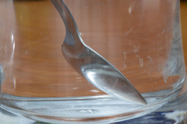 Metalen lepel in lege glazen beker. Kalkvlekken ingesmeerd met water op glas. Close-up. - Foto, afbeelding