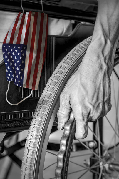 Senior en silla de ruedas en el hogar de ancianos en blanco y negro con colgar la máscara de la bandera de los Estados Unidos en color. Concepto de brote de coronavirus Covid-19 en hogares de ancianos estadounidenses o centros de retiro para ancianos
. - Foto, imagen