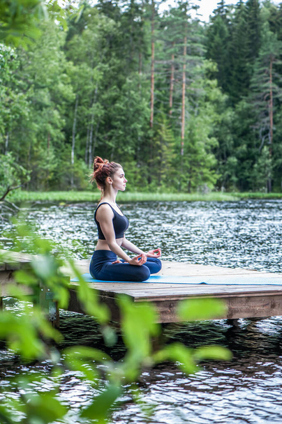 Красивая девушка в позе йоги на озере. Позиция лотоса, Падмасана. Концепция умиротворения, здорового образа жизни. Панорамный вид
 - Фото, изображение