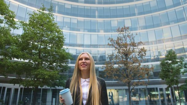 Stylish business woman with coffee on street. From below of serious blond executive young woman in suit having coffee in paper cup looking away on street. - Фото, изображение