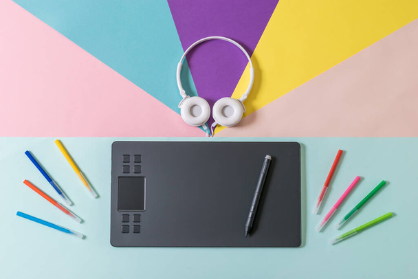 Scattered markers, white headphones, and a graphic tablet on a multicolored background. - Photo, Image