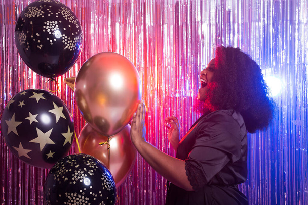 Portret van een mooie Afro-Amerikaanse vrouw tegen twinkelende achtergrond. Verjaardagsfeest, nachtclub en nachtleven concept. - Foto, afbeelding