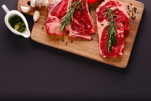 Fresh raw beef steak on wooden cutting board over black background with spices, top view. - Foto, immagini