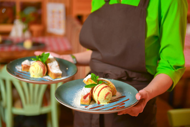 Close up of waitress serving apple strudel with vanilla ice cream and mint on blue plate. Restaurant or cafe service. - Foto, Bild