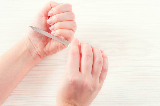Ruka bílé ženy se zdravými přírodními nehty Získávání péče o nehty. Bílé ženské ruce leští nehty pilníkem na nehty, izolovaný na bílém dřevěném pozadí. Krása manikúra. - Fotografie, Obrázek