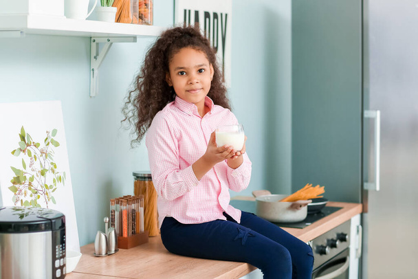Pequena menina afro-americana com leite na cozinha
 - Foto, Imagem