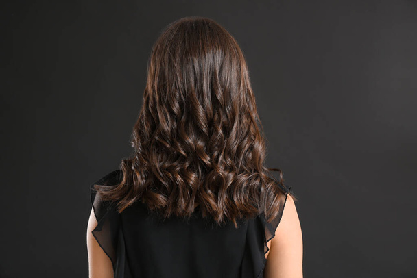Νεαρή γυναίκα με όμορφα σγουρά μαλλιά σε σκούρο φόντο - Φωτογραφία, εικόνα