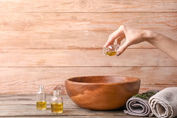 Woman pouring essential oil from bottle into bowl on wooden background - Fotografie, Obrázek