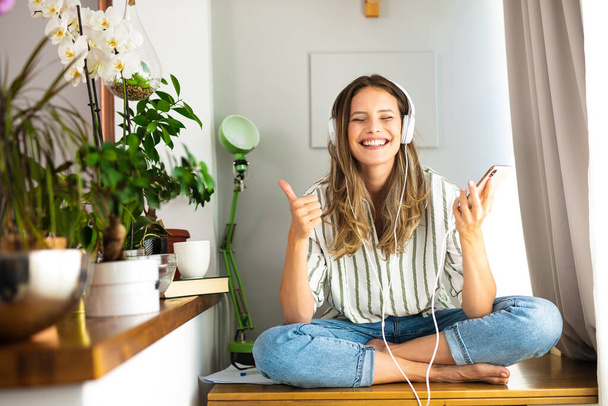 happy single woman comunicating and listening music on the desk next to the plants and bright window, work from home, stay at home. - Фото, зображення