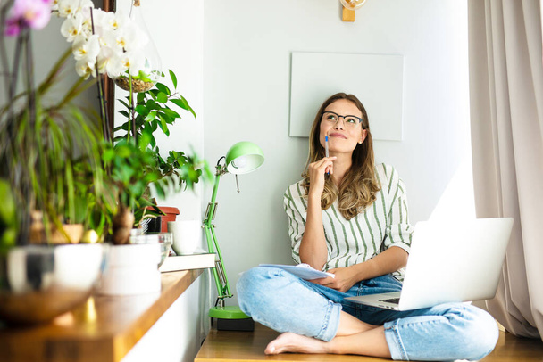 work from home or studding online, concept with a woman working at laptop inside the house, next to a bright window and the houseplant - Foto, Imagen