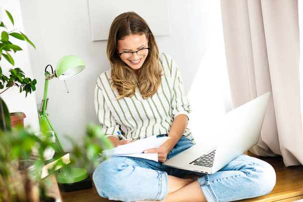 work from home or studding online, concept with a woman working at laptop inside the house, next to a bright window and the houseplant - Zdjęcie, obraz