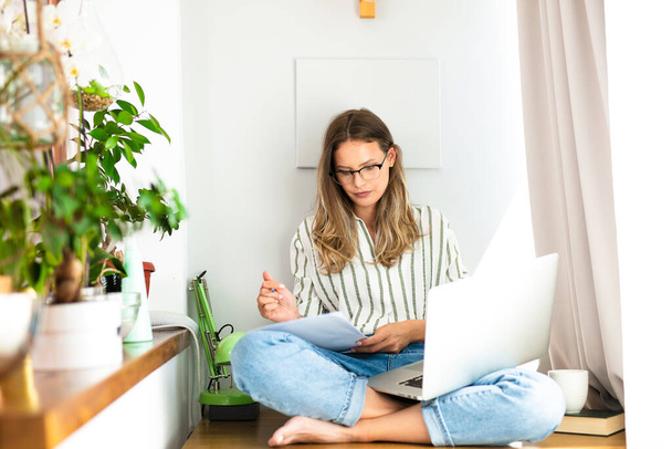 work from home or studding online, concept with a woman working at laptop inside the house, next to a bright window and the houseplant - Фото, зображення