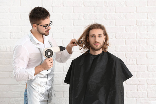 Junger Friseur arbeitet mit Kundin vor weißem Backsteinhintergrund - Foto, Bild