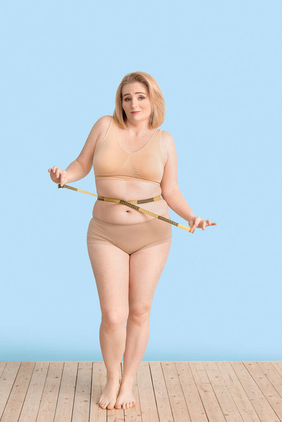 Mujer triste con sobrepeso con cinta métrica en el fondo de color. Concepto de pérdida de peso
 - Foto, imagen