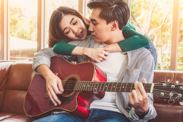 Junges asiatisches Paar spielt gemeinsam Gitarre und singt im Wohnzimmer. Musik- und Lifestyle-Konzept. - Foto, Bild