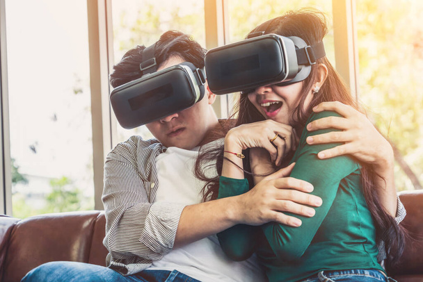 自宅のリビングルームで仮想現実VRヘッドセットでビデオを見て幸せなカップル。マルチメディア映画とエンターテイメントのコンセプト. - 写真・画像