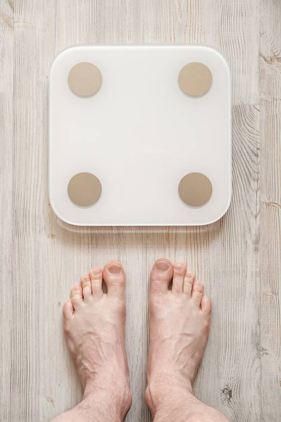 Male bare feet stand next to smart scales that makes bioelectric impedance analysis, BIA, body fat measurement. Top view. - Photo, Image