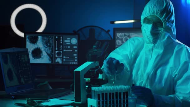Suojapukuinen tutkija ja tutkimuslaboratoriossa laboratoriolaitteilla työskentelevät naamiot: mikroskoopit, koeputket. Coronavirus 2019-ncov vaara, lääketieteellinen löytö, bakteriologia ja virologia
 - Materiaali, video