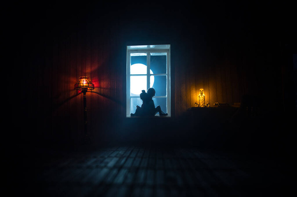 Realistický obývací pokoj pro panenky s nábytkem a oknem v noci. Romantický pár sedí na okně. Dekorace uměleckého stolu s ručně vyrobeným realistickým domečkem pro panenky. Selektivní zaměření. - Fotografie, Obrázek