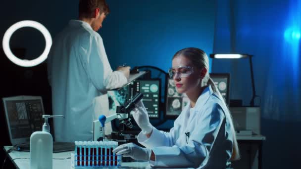 Lékařští vědci pracující v laboratoři. Doktor učí stážisty analyzovat krev. Laboratorní nástroje: mikroskop, zkumavky, vybavení. Koronavirus, biotechnologie, bakteriologie, virologie a - Záběry, video