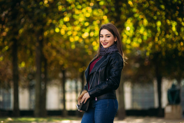 Stylish beautiful lady in a black leather jacket with a black bag. Attractive young woman smile - Photo, Image
