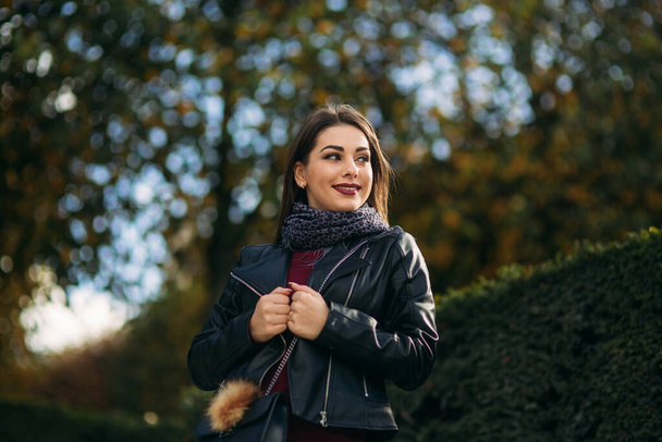 Stylish beautiful lady in a black leather jacket with a black bag and burgundy blouse. Attractive young woman smile - Fotografie, Obrázek