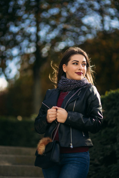 Stylish beautiful lady in a black leather jacket with a black bag and burgundy blouse. Attractive young woman smile - Фото, зображення