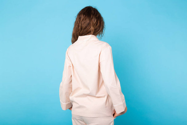 Young girl posing in pajamas on blue background. Relax good mood, lifestyle and sleepwear concept. Back view. - Foto, imagen