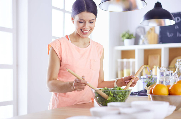 Smiling young woman mixing fresh salad in the kitchen. - Φωτογραφία, εικόνα