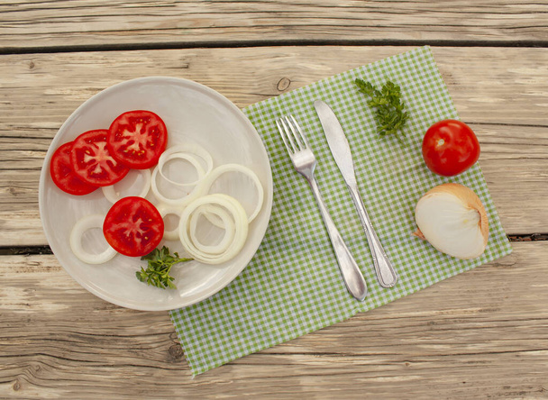verdure, un piatto con verdure tritate, un coltello da tavola e una forchetta su un tovagliolo di tessuto su un tavolo in giardino, vista dall'alto.
. - Foto, immagini