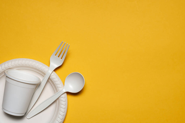 disposable plate, glass, spoon and fork of corn starch on a yellow background. biodegradable eco friendly picnic tableware. isolate. replacement of plastic with modern biomaterials. place for text - Photo, Image
