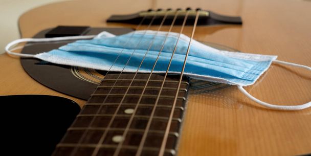 Una maschera medica blu giace su una chitarra acustica. Concetto musicale di Coronavirus
. - Foto, immagini