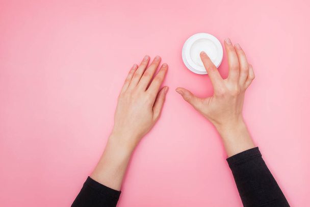 Woman moisturizing her hand with cosmetic cream with copy space on pink background in minimalism style. - 写真・画像