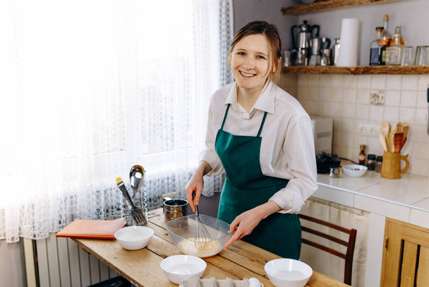 Щаслива молода жінка готує тісто для торта на кухні. Кулінарія в домашніх умовах концепція
. - Фото, зображення