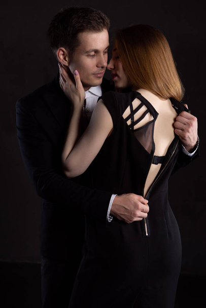 An elegant man unzips the dress of a girl who is kissing him, exposing her slender sexy back. The girl gently strokes the man's cheek during a kiss - Foto, Imagen