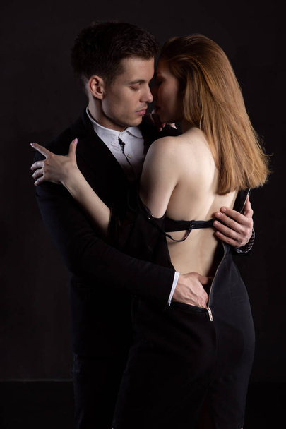 An elegant man in love undresses a woman during a passionate embrace. A man with pleasure touches the ass of his favorite woman. Passionate couple undressing on a dark background - Photo, Image