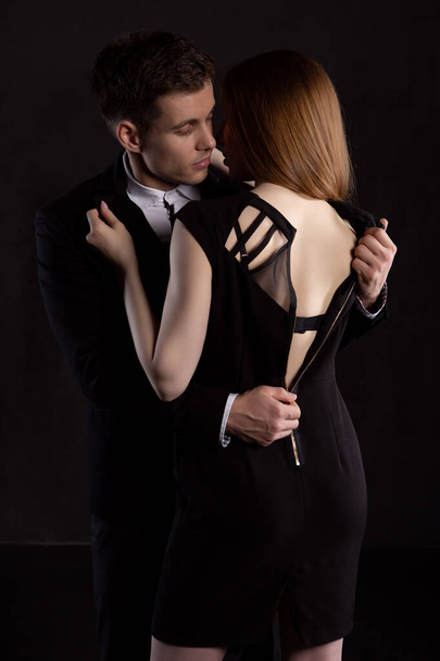 Fashionable portrait of an elegant sexy couple in the Studio. An elegant man in a suit unbuttons his girlfriend's dress during a hug, exposing her beautiful back - Foto, Bild