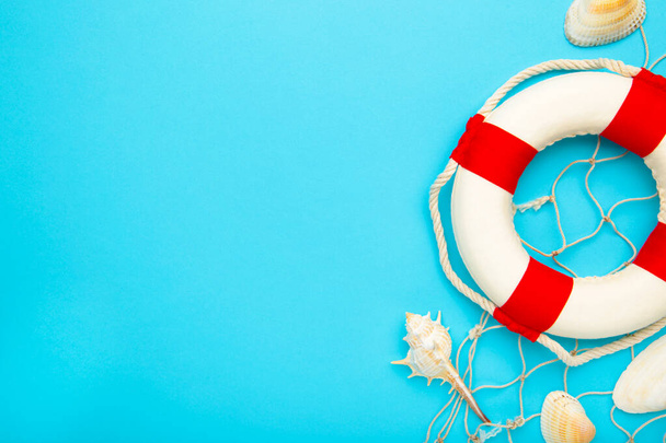 Red-white lifebuoy with seashells on blue background. Top view - Photo, Image