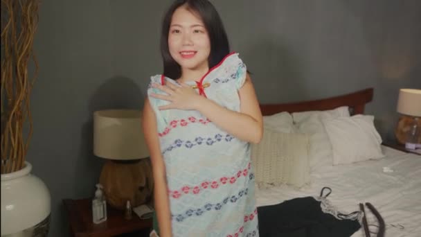 home lifestyle portrait of young happy and sweet Asian Japanese woman trying different clothes and new dress looking in bedroom mirror deciding what to wear for her date - Filmati, video