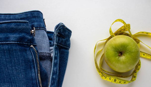 Blauwe jeans, een groene Apple en een centimeter op een witte achtergrond.Gewichtsverlies en het concept van gewichtsverlies. - Foto, afbeelding