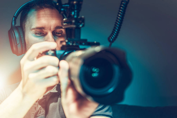 Biały operator kamery w wieku 30 lat, robiący zdjęcia filmowe przy użyciu nowoczesnej lustrzanki. Filmowiec w pracy. - Zdjęcie, obraz