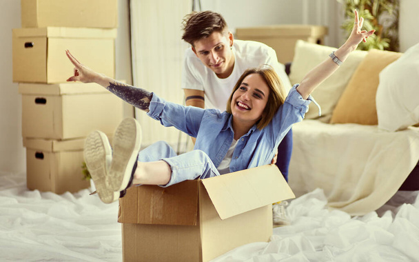 Happy couple having fun and riding in cardboard boxes at new home - Foto, immagini