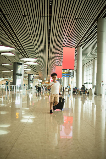 Portrait of young adorable little boy running in airport with him black suitcase - Photo, Image