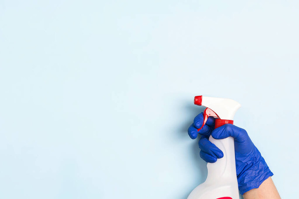 Hand in medical glove holds a bottle with antiseptic spray on a blue background. Disinfectant concept. Coronavirus precaution. - Foto, afbeelding