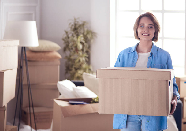 Portrait of pretty woman holding a box at new home - 写真・画像
