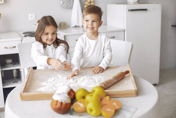 Cute little children sitting in a kitchen with dough - Fotó, kép